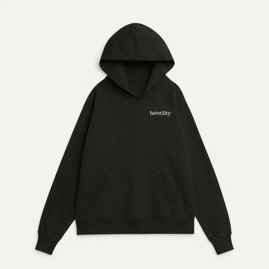front view of black oversized organic french terry hoodie with "hotstility" embroidered text on chest, relaxed fit with structured silhouette